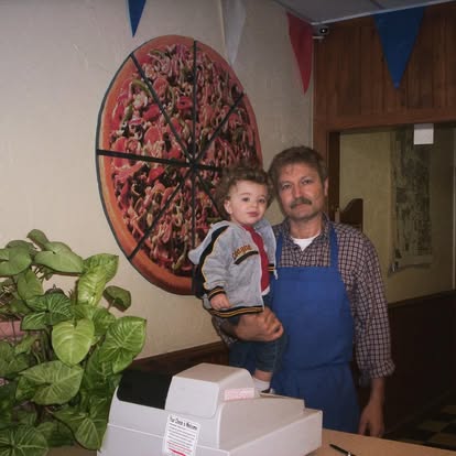 A guy behind a counter holding a kid.