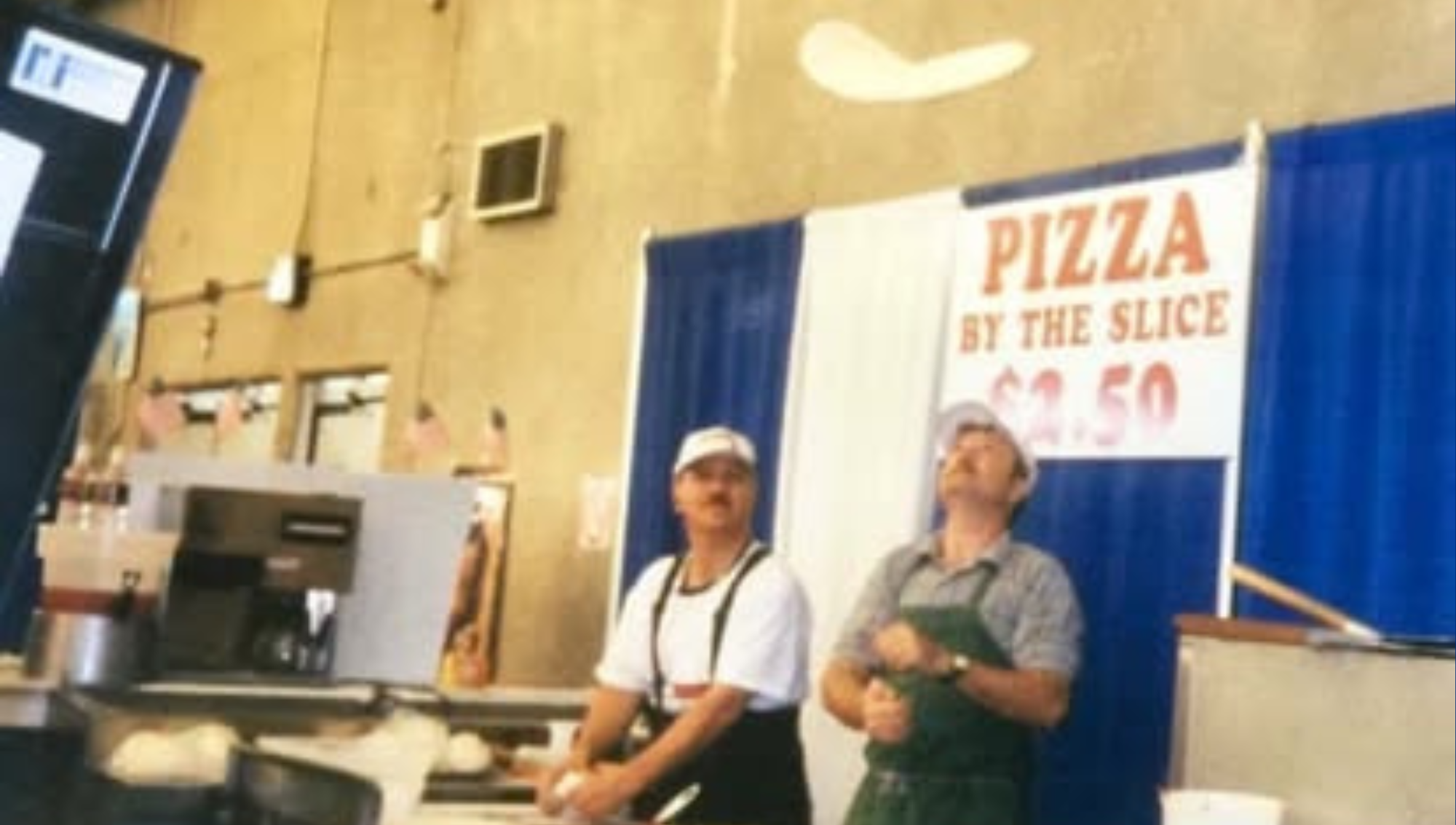 Two guys at a fair booth selling pizza by the slice.